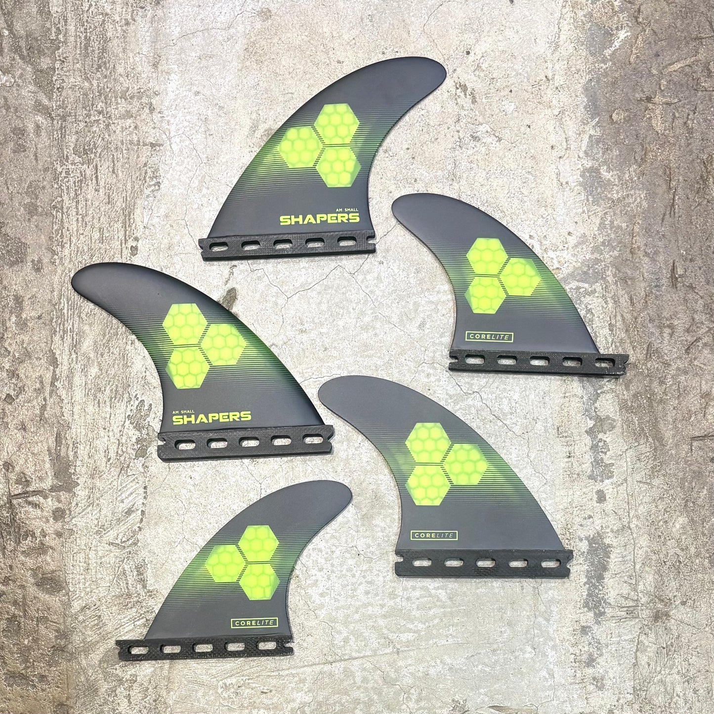 Five surfboard fins with green geometric pattern on a textured surface