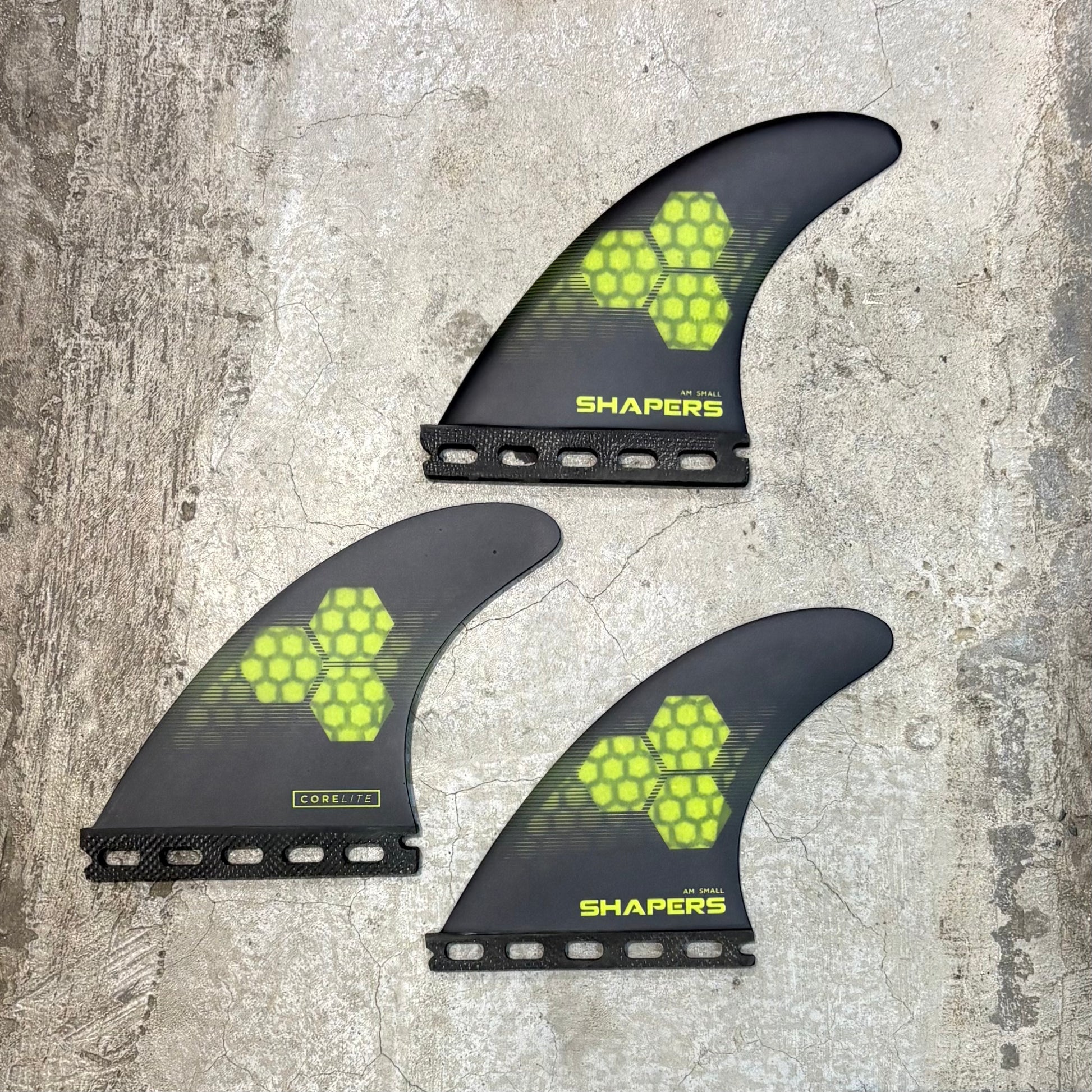 Three surfboard fins with 'Shapers' branding on a textured surface