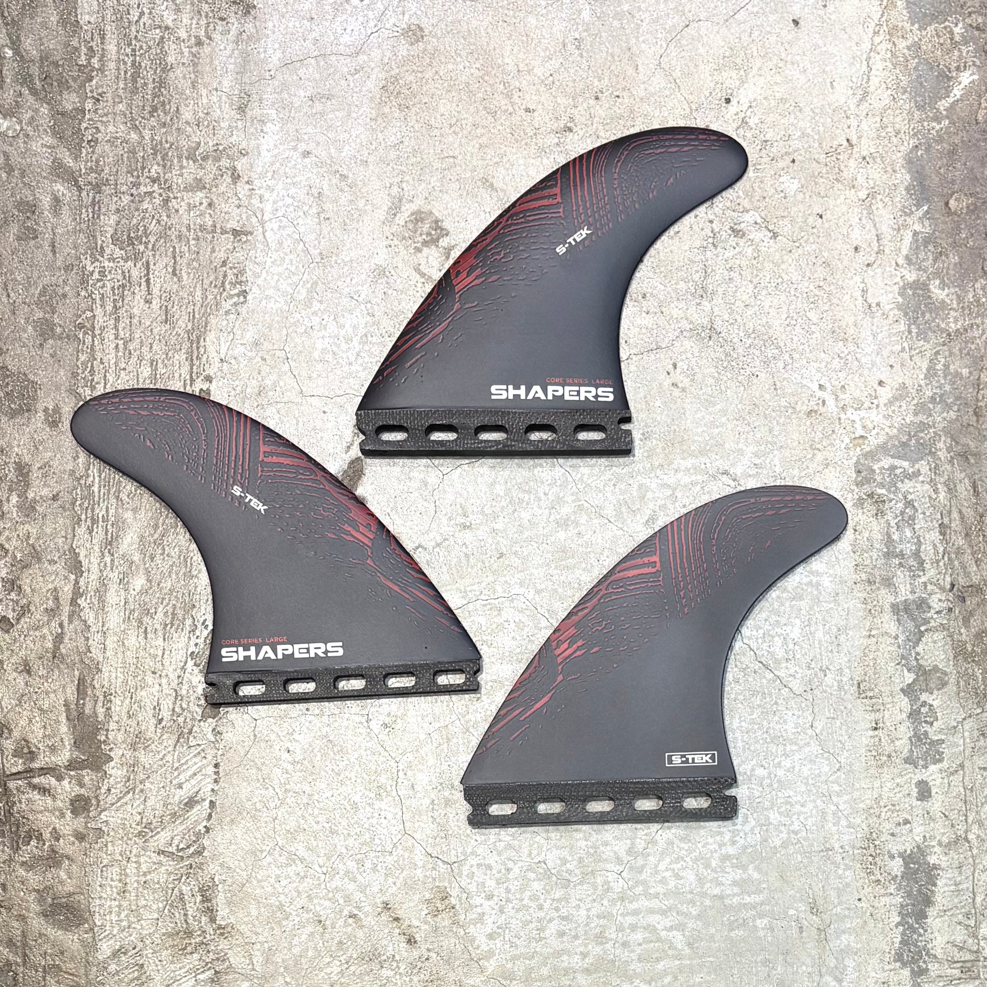 Three surfboard fins with 'Shapers' branding on a textured surface
