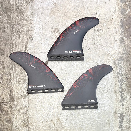 Three surfboard fins with 'Shapers' branding on a textured surface