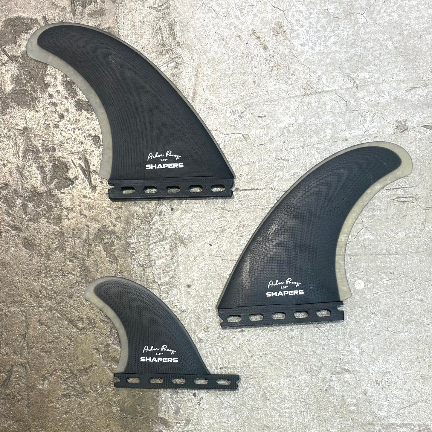 Three black surfboard fins with 'Surf City Shapers' branding on a textured surface.