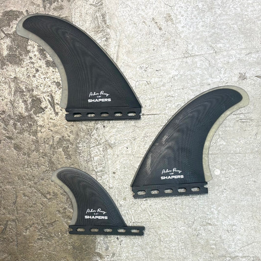 Three black surfboard fins with 'Surf City Shapers' branding on a textured surface.