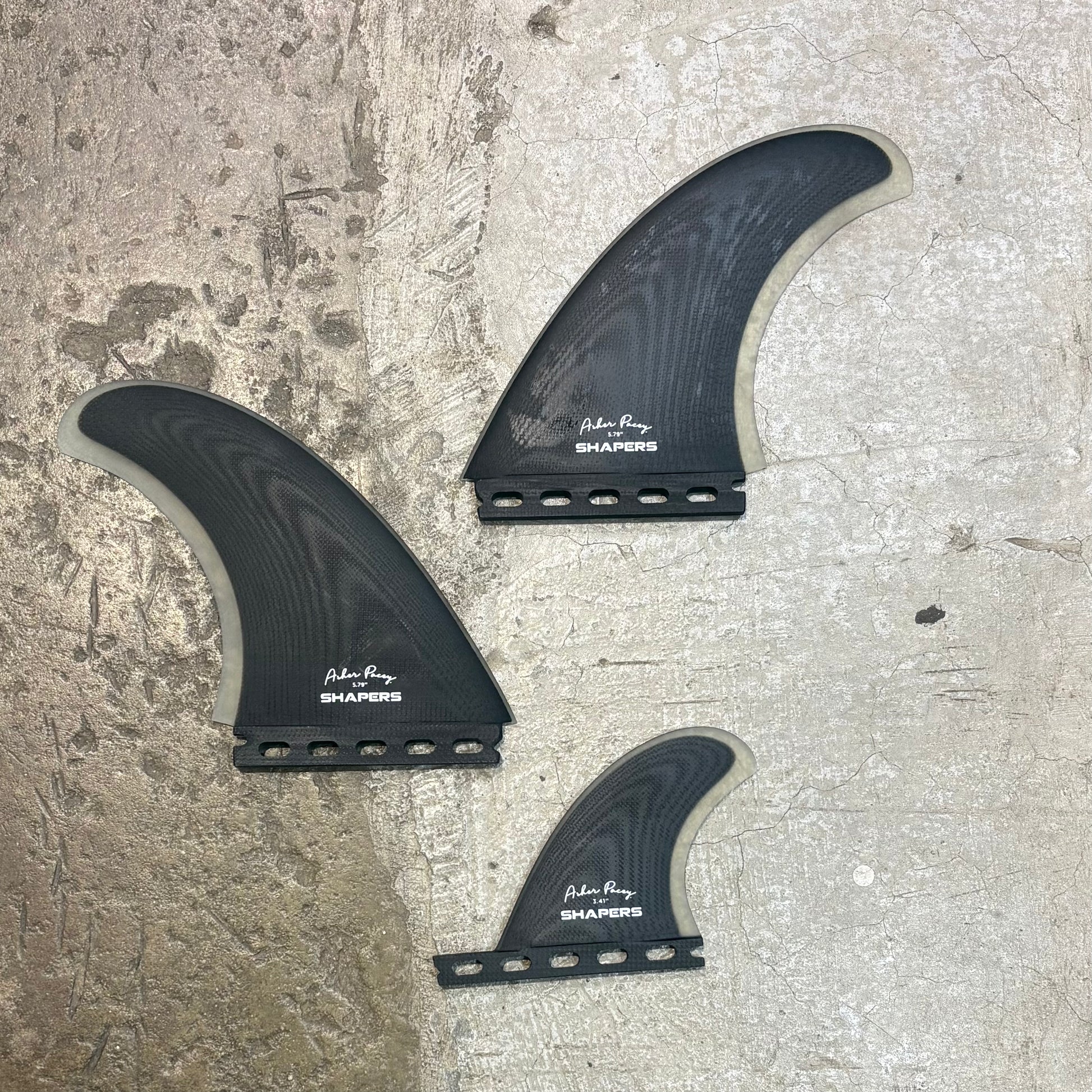 Three black surfboard fins with 'Parker Ring Shapers' branding on a textured surface.