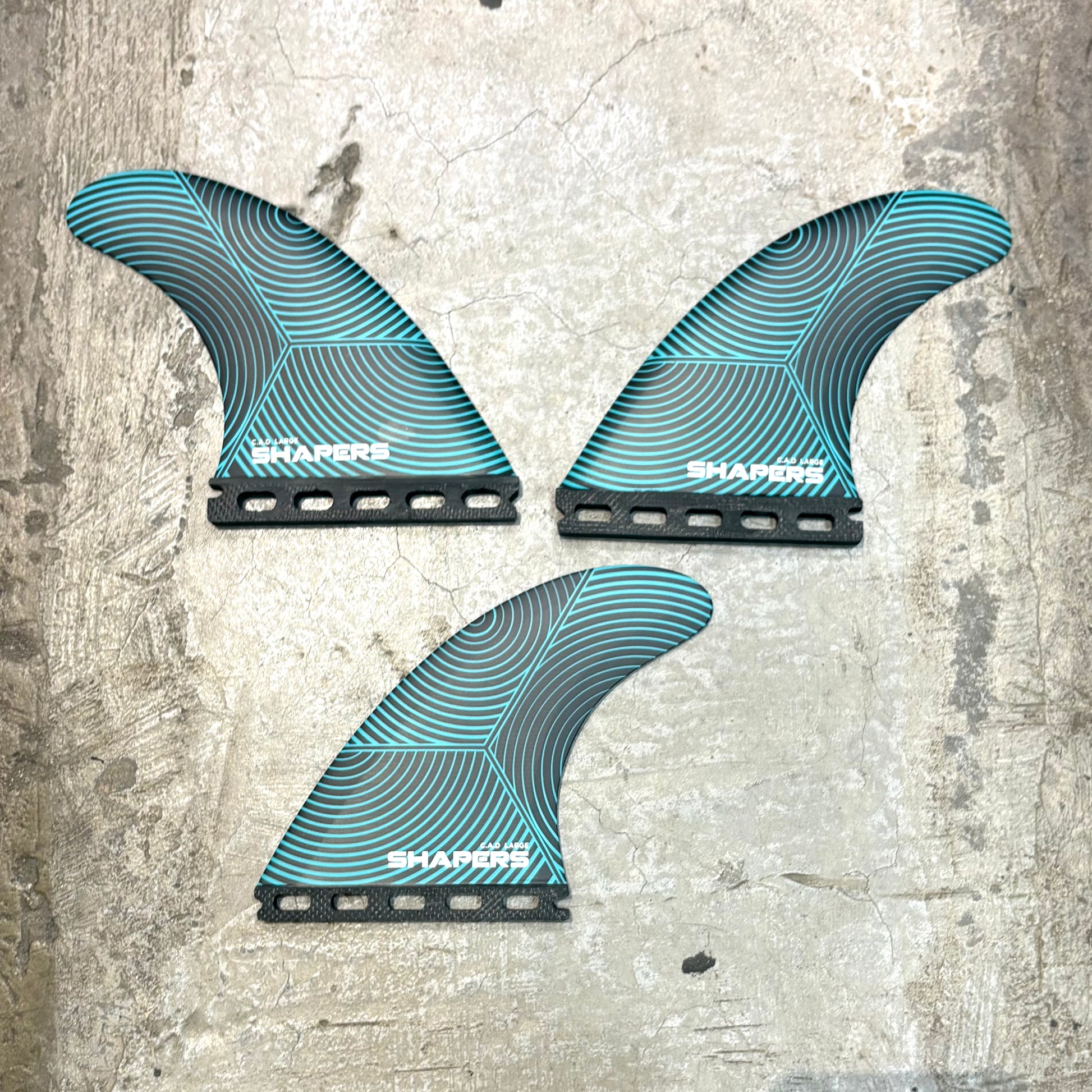 Three blue and black surfboard fins on a textured surface