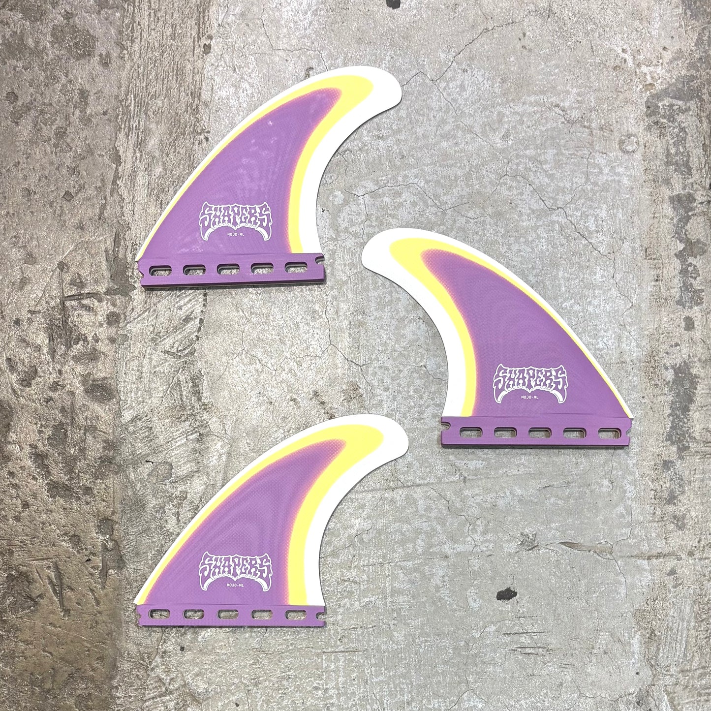 Three purple and yellow surfboard fins on a textured gray surface