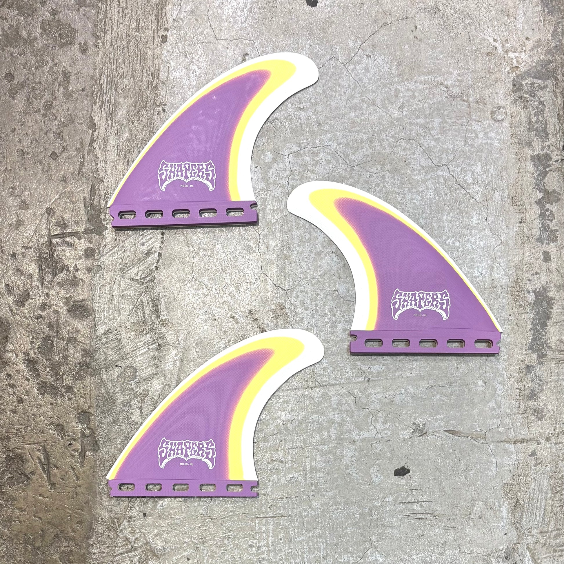 Three purple and yellow surfboard fins on a textured gray surface