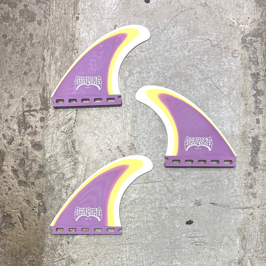 Three purple and yellow surfboard fins on a textured gray surface