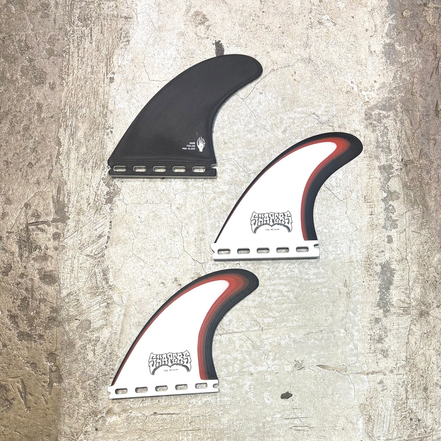 Three surf fins with a brand logo on a textured surface