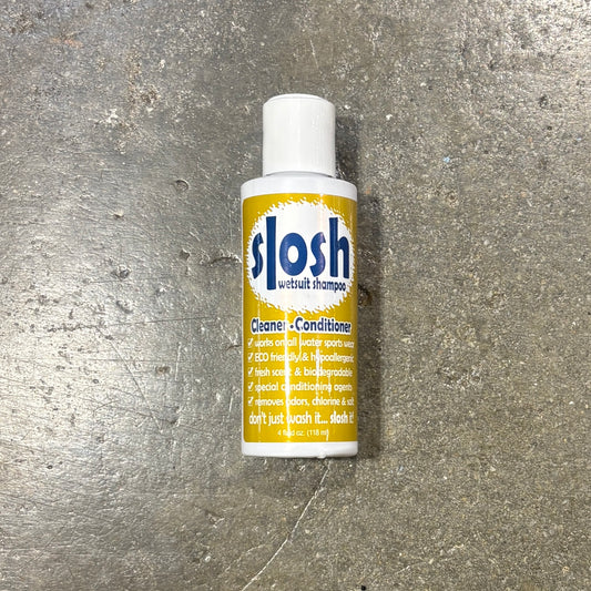 A bottle of slosh withhair shampoo cleaner and conditioner placed on a textured gray concrete surface. The bottle is white with a yellow label and blue slosh branding.