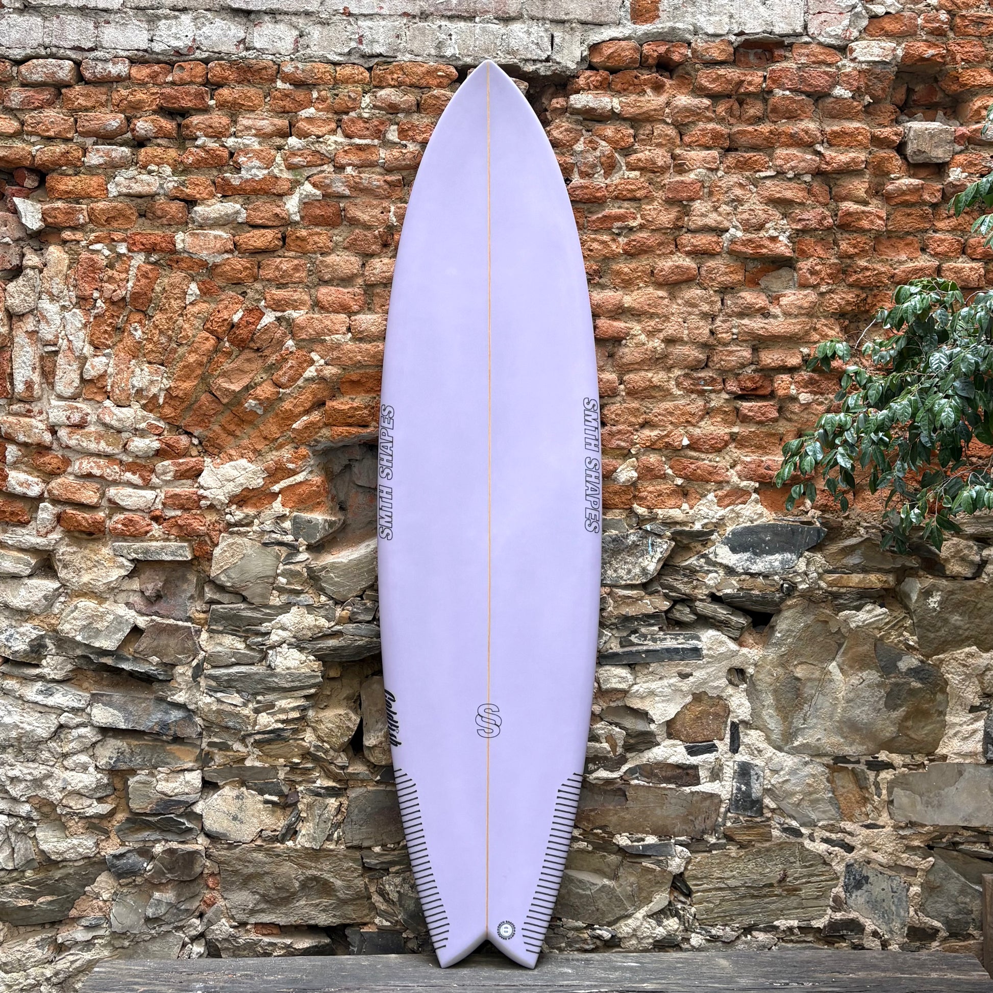 Purple SMTH surfboard leaning against a textured stone wall.