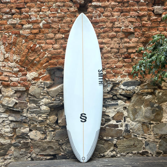 White Smith surfboard with a logo against a rustic stone wall