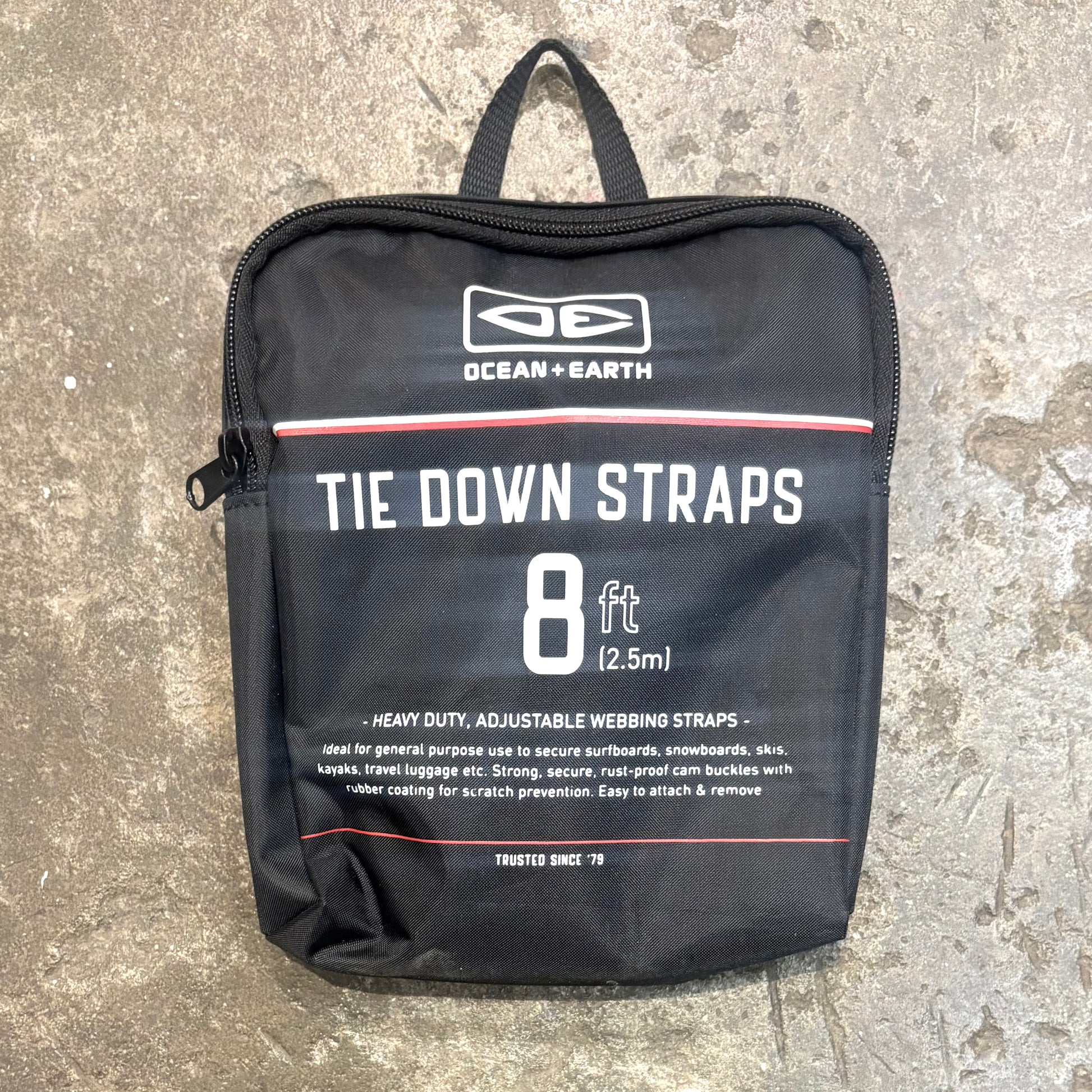 Black bag with 'Ocean + Earth' branding containing tie-down straps on a concrete surface.