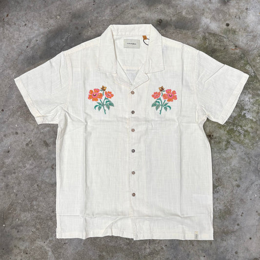 White short-sleeve shirt with floral embroidery on a concrete surface