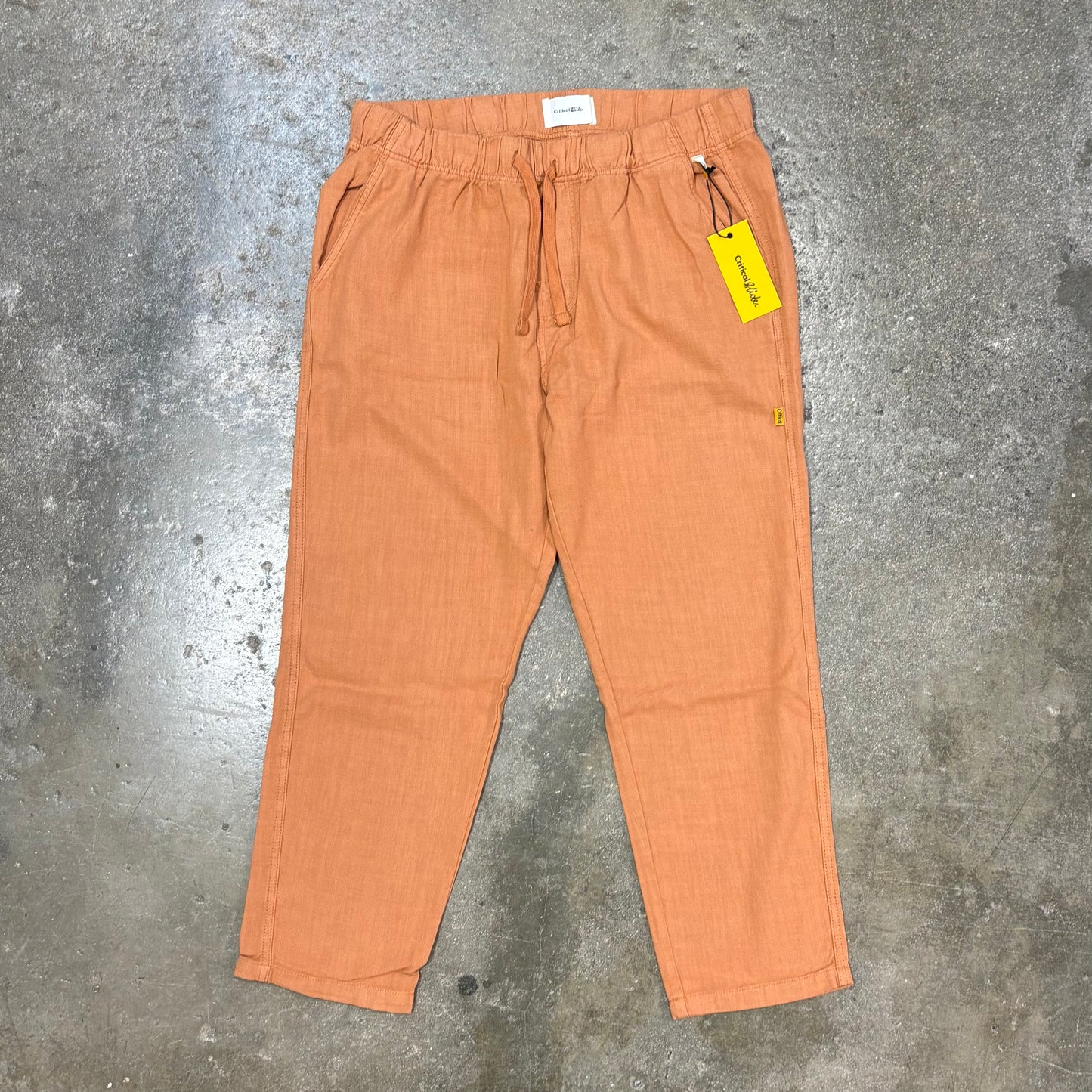 Orange pants with a yellow tag on a textured gray surface