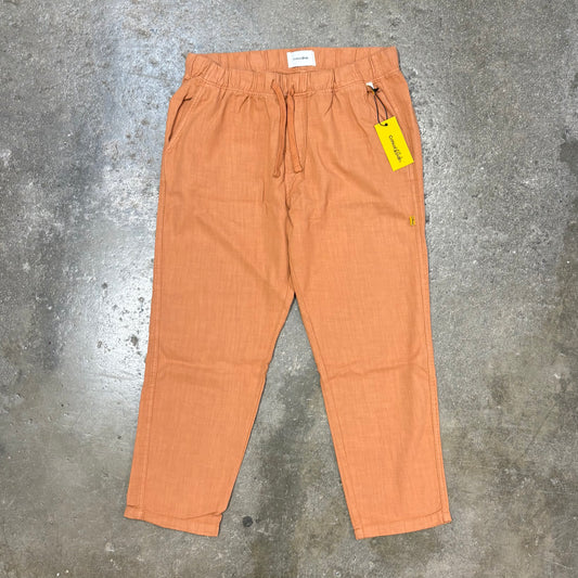 Orange pants with a yellow tag on a textured gray surface