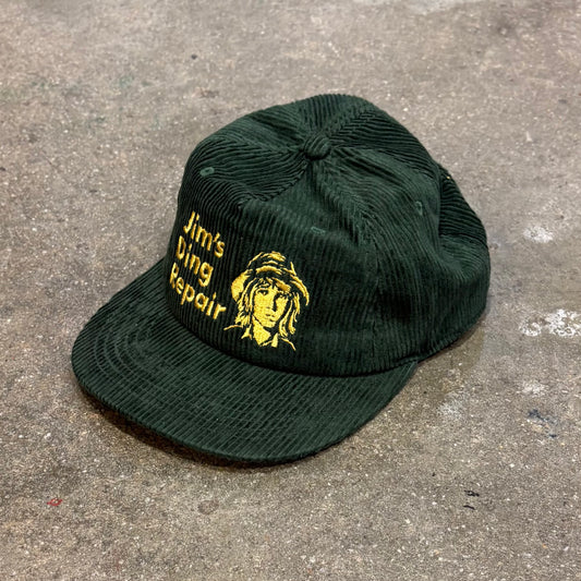 Green cap with embroidered design and text on a concrete surface