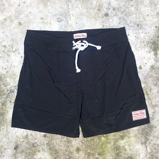 Black board shorts with a white drawstring and a visible 'Historic Roads' brand patch, laid flat on a textured concrete surface.
