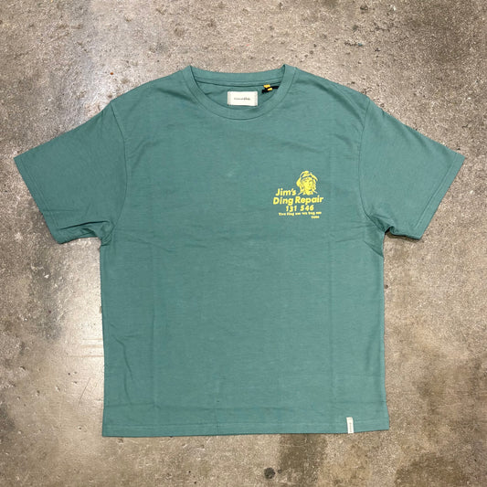 Green t-shirt with yellow text and logo on a concrete surface