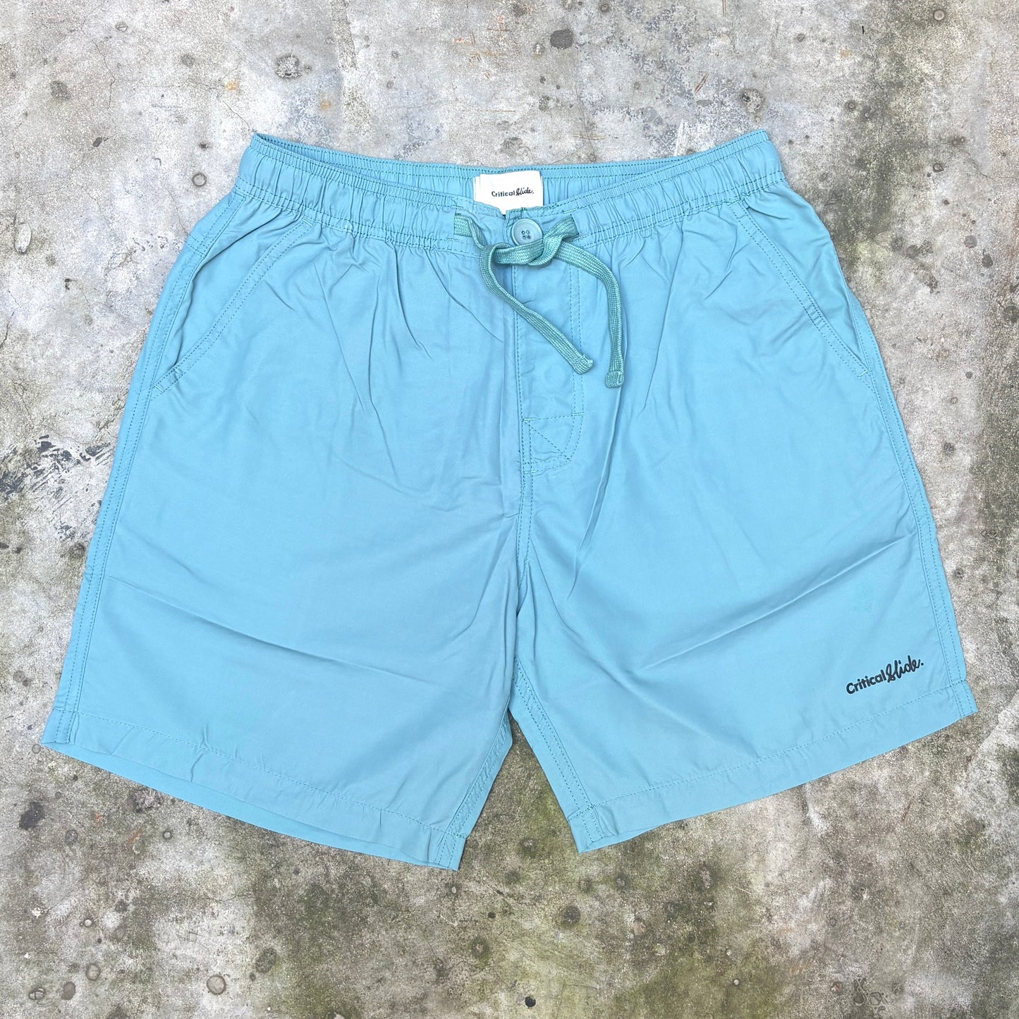 Light blue drawstring shorts laid flat on a textured concrete surface, with a small black 'oneokids' logo on the lower right leg.
