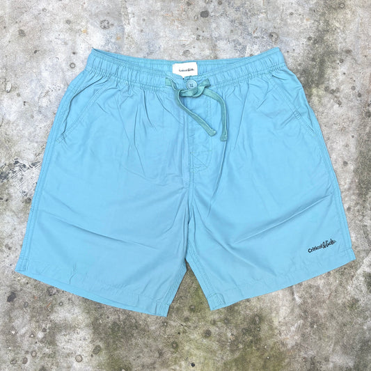 Light blue drawstring shorts laid flat on a textured concrete surface, with a small black 'oneokids' logo on the lower right leg.
