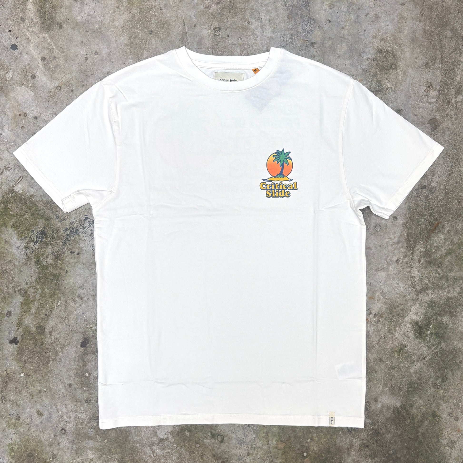 A white short-sleeve crewneck t-shirt with a small colorful chest graphic featuring a palm tree and the text 'Carmen Hills', laid flat on a textured gray concrete surface.