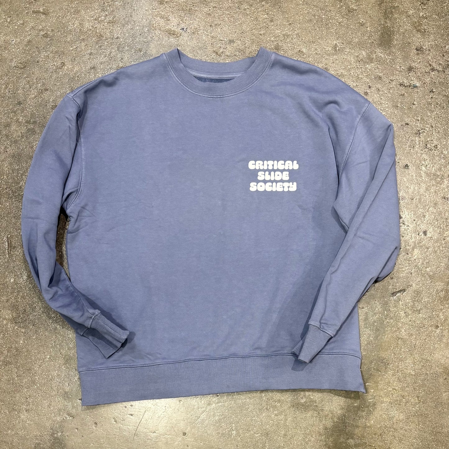 Blue sweatshirt with 'Critical Slide Society' text on a concrete surface