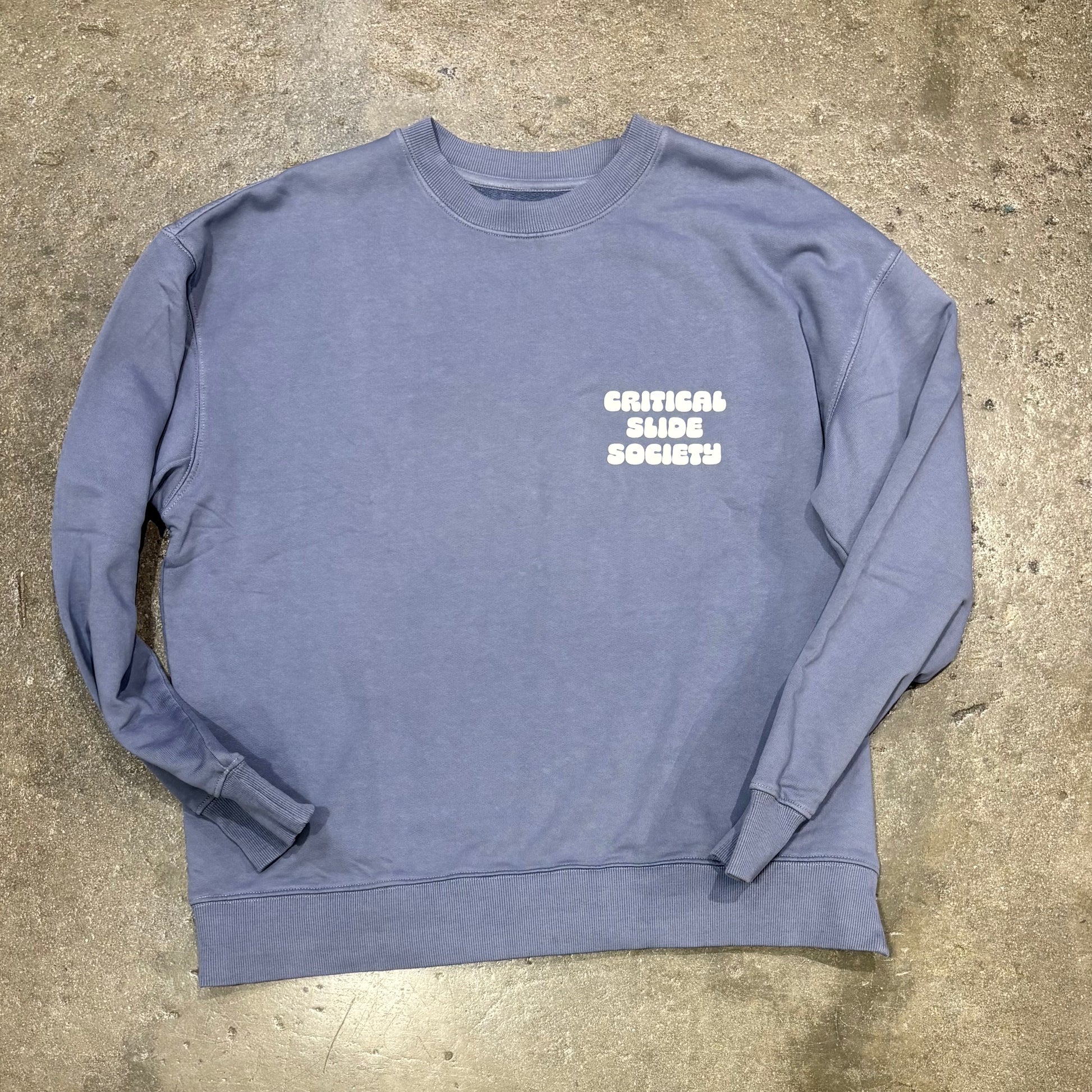 Blue sweatshirt with 'Critical Slide Society' text on a concrete surface