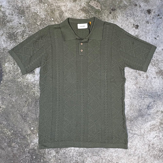 Green patterned polo shirt on a textured gray surface