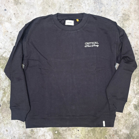 A black crewneck sweatshirt with 'CRITICAL Design' embroidered in white on the left chest, laid flat on a textured concrete surface.