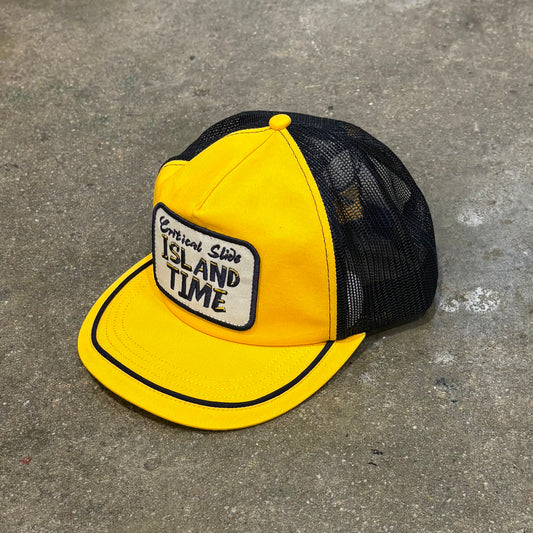 Yellow and black cap with 'Island Time' patch on a concrete surface