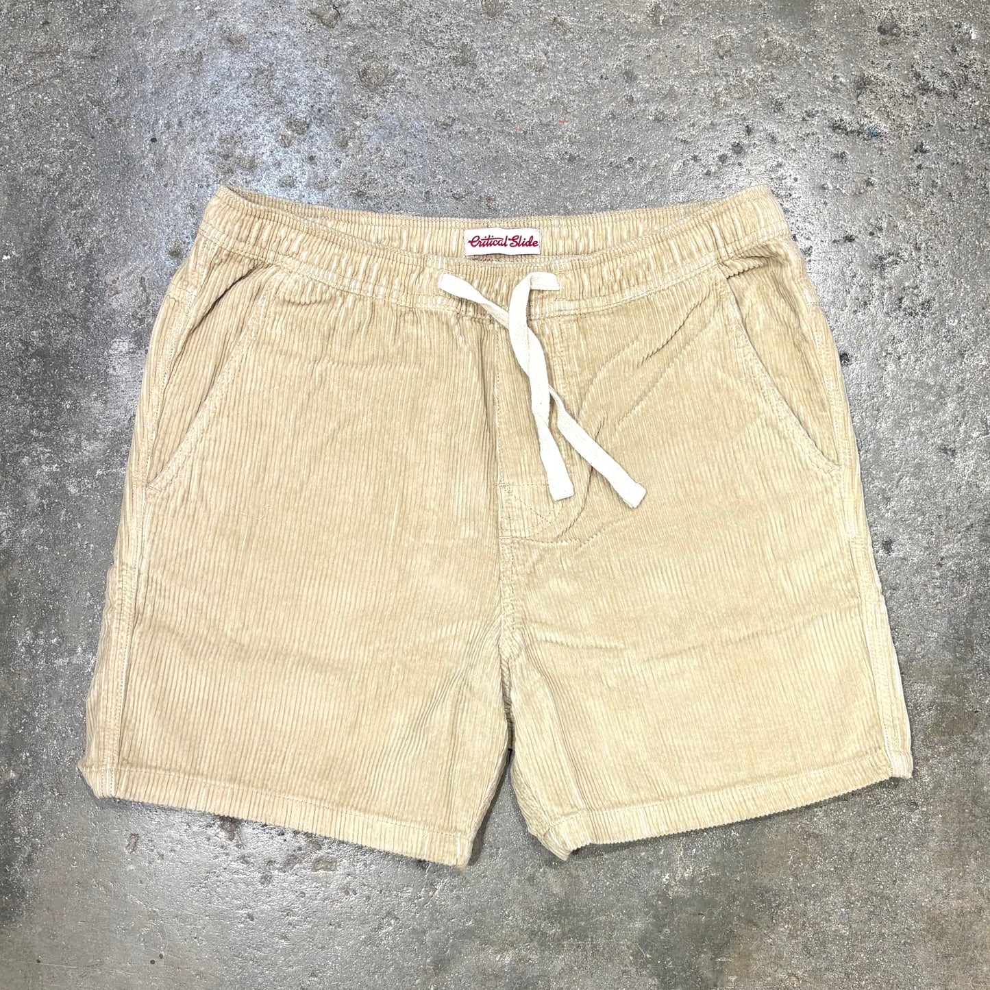 Beige shorts with a white drawstring on a gray concrete surface
