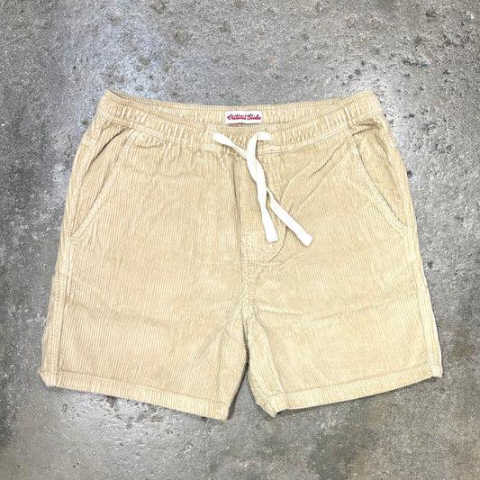 Beige shorts with a white drawstring on a gray concrete surface