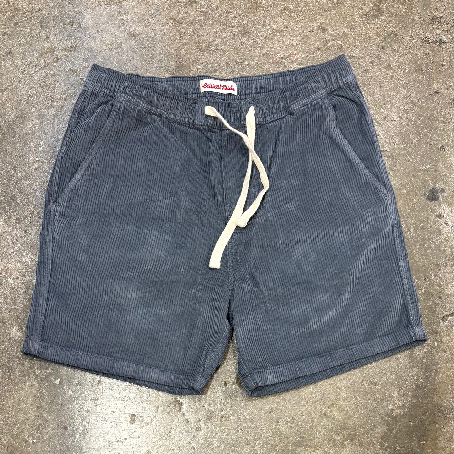 Blue corduroy shorts with a drawstring on a concrete surface