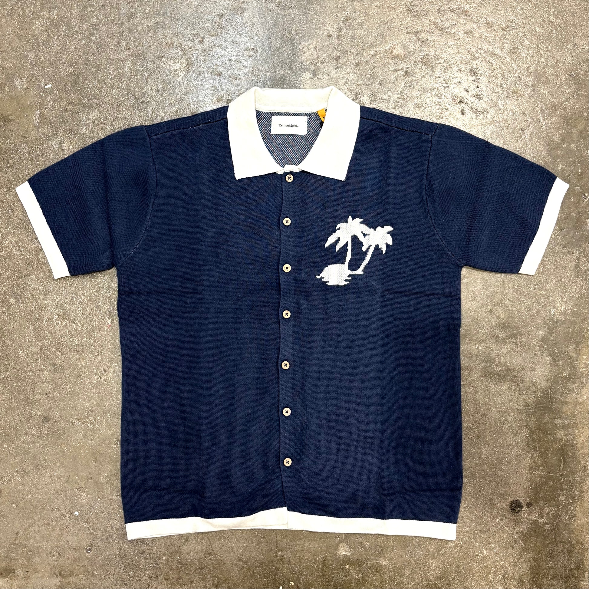 Navy blue shirt with white collar and palm tree design on a textured surface