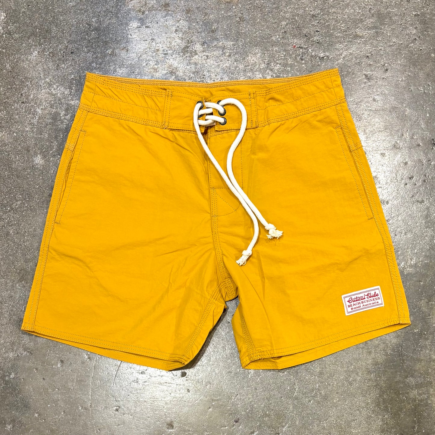 Yellow shorts with a white drawstring on a gray concrete surface