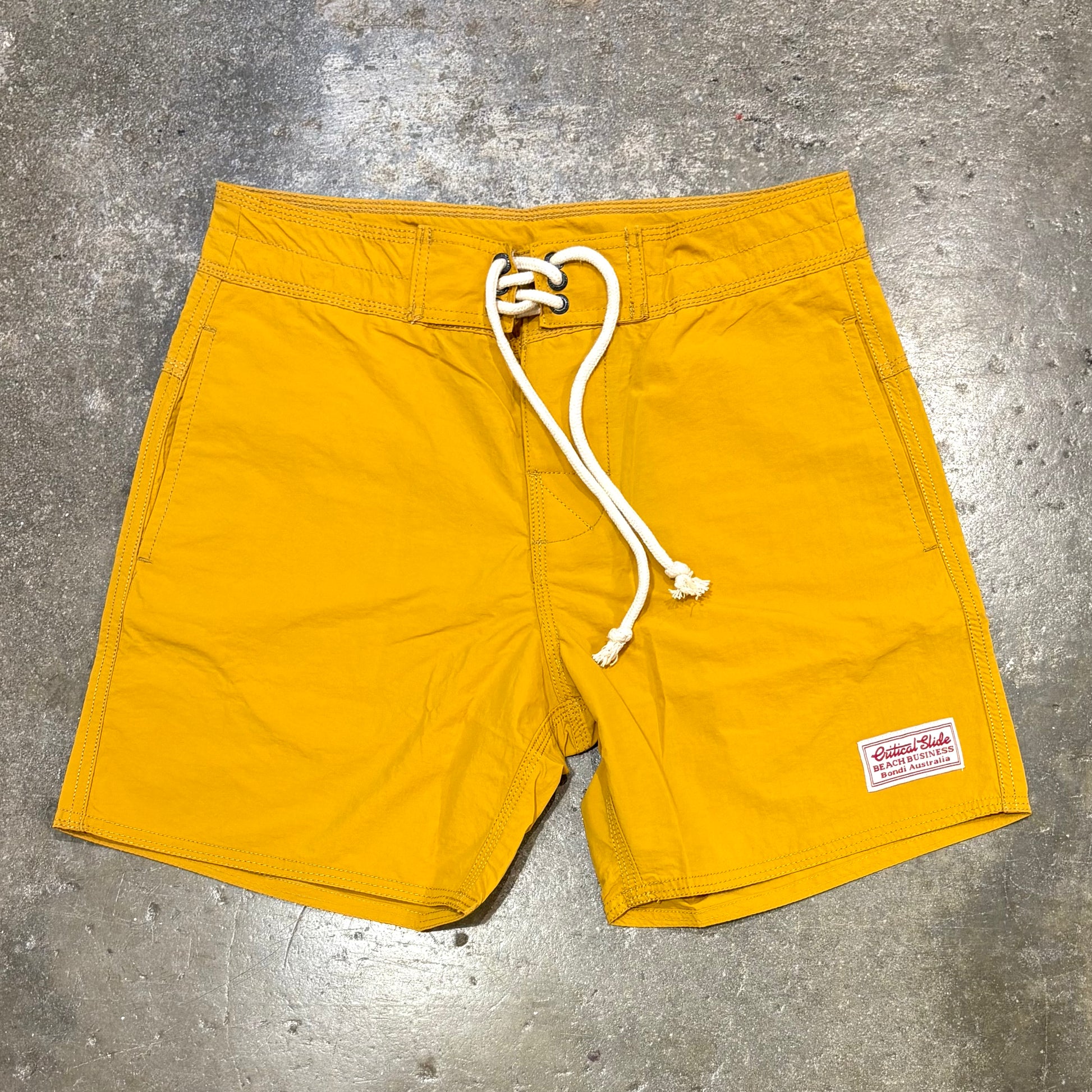 Yellow shorts with a white drawstring on a gray concrete surface