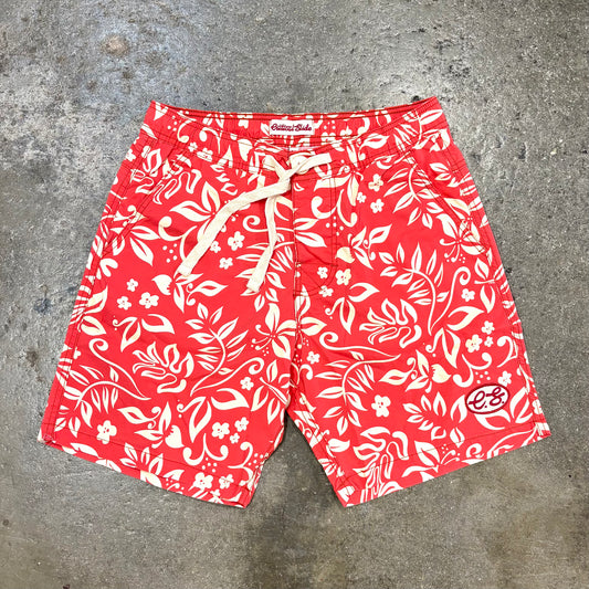 Red swim shorts with white floral pattern on a concrete surface