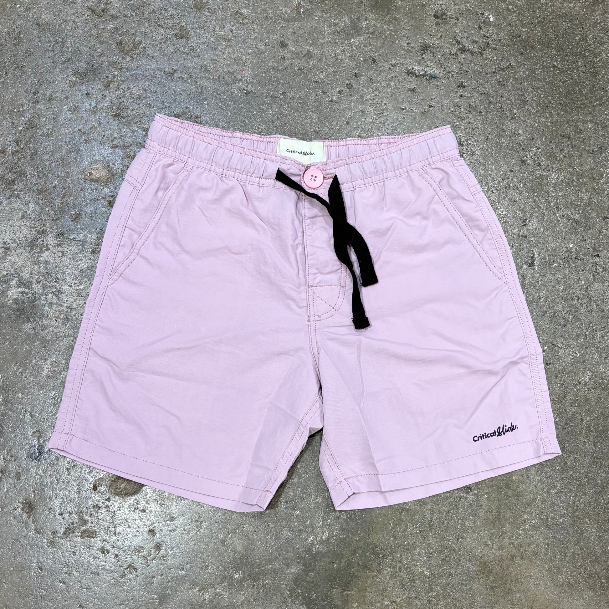 Light purple shorts with a black drawstring on a concrete surface