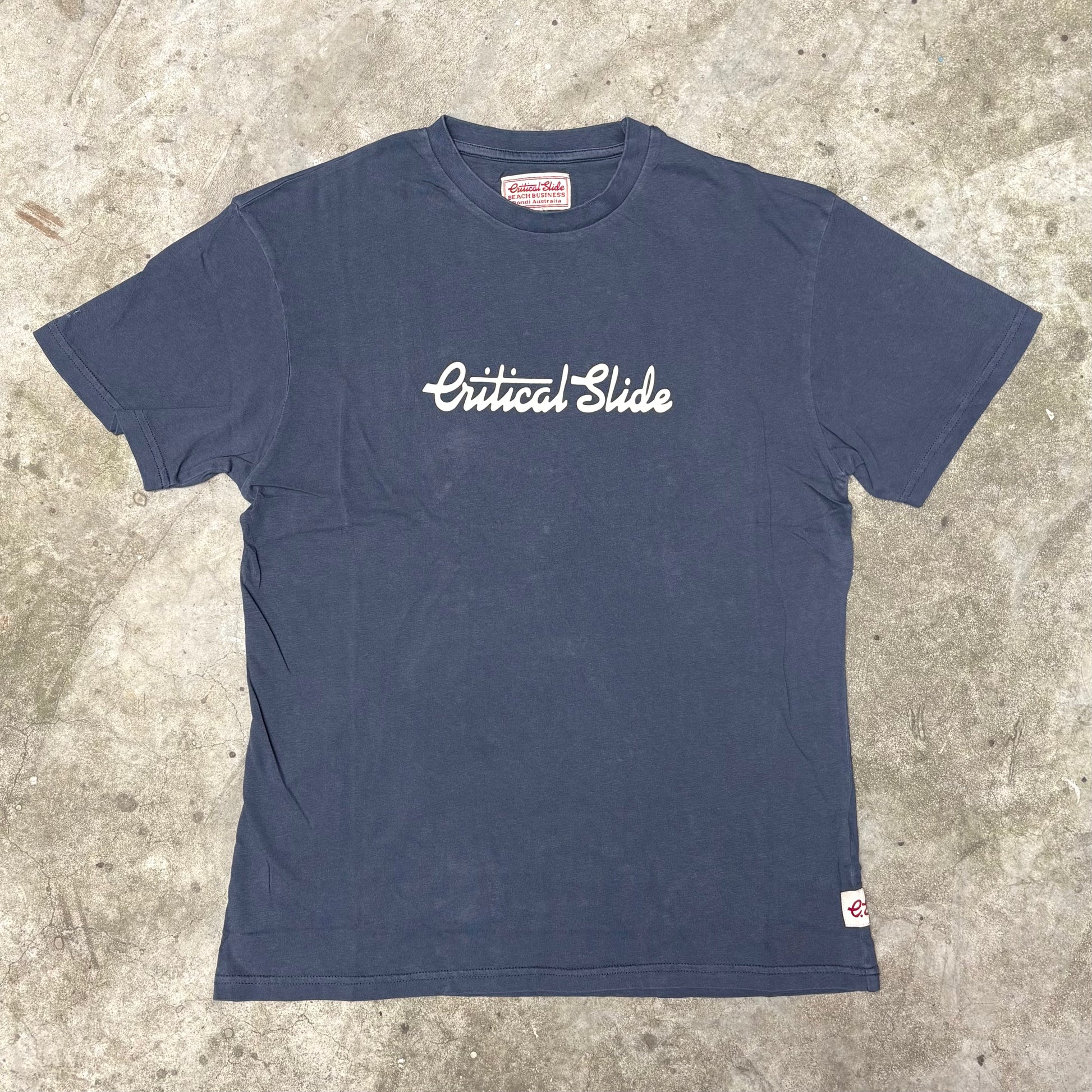Navy blue t-shirt with 'Critical Slide' logo on a concrete surface
