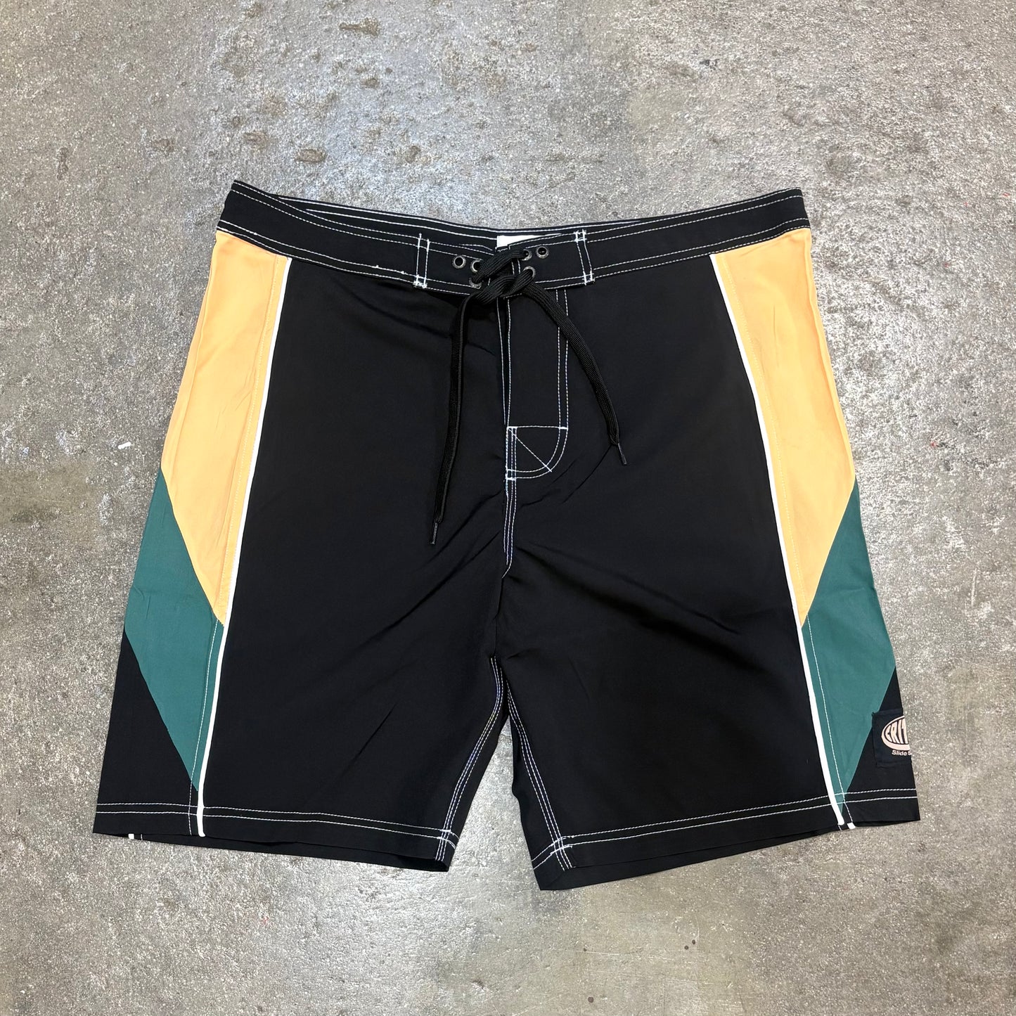 Black shorts with yellow and green accents on a concrete surface