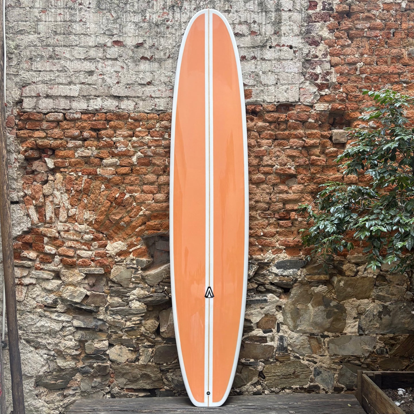 Orange surfboard with a white stripe against a rustic stone wall.