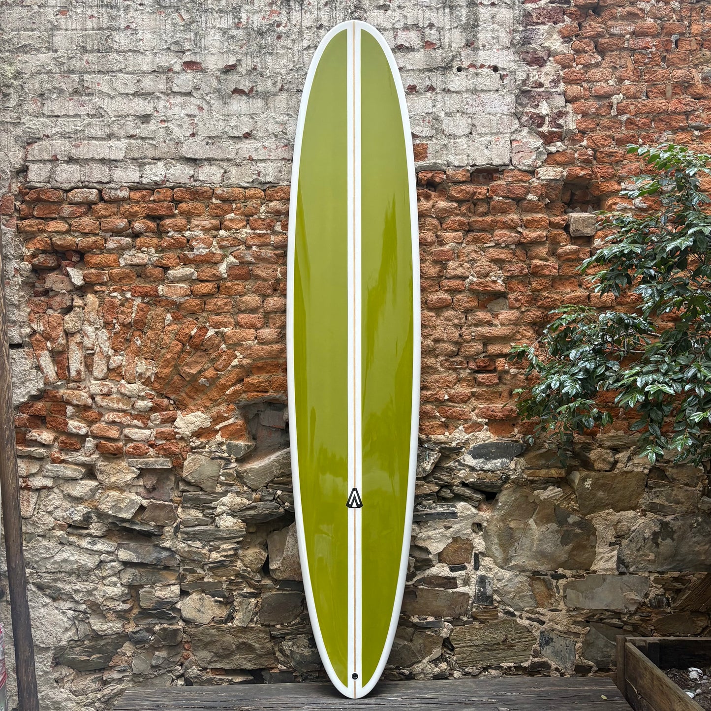 Green Analogy Surfboard  with a white stripe against a rustic stone wall.