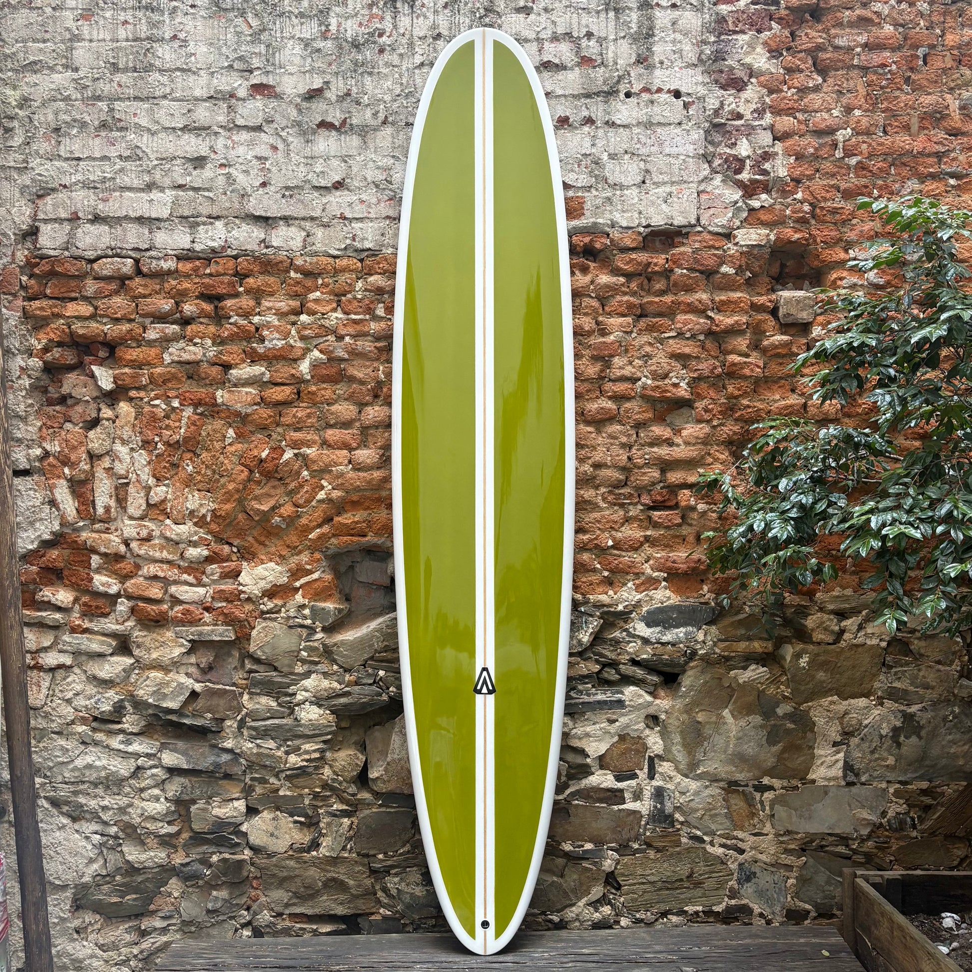 Green Analogy Surfboard  with a white stripe against a rustic stone wall.