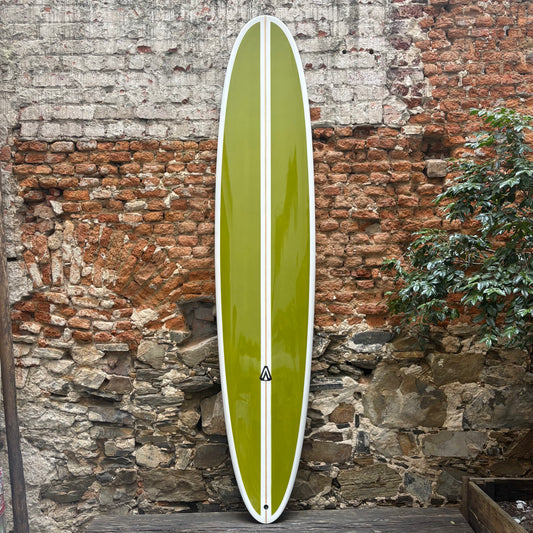 Green Analogy Surfboard  with a white stripe against a rustic stone wall.