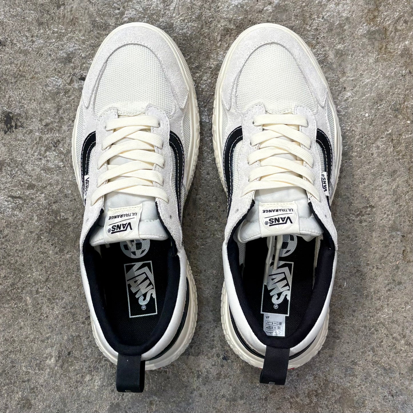 Pair of white sneakers with black accents on a concrete surface
