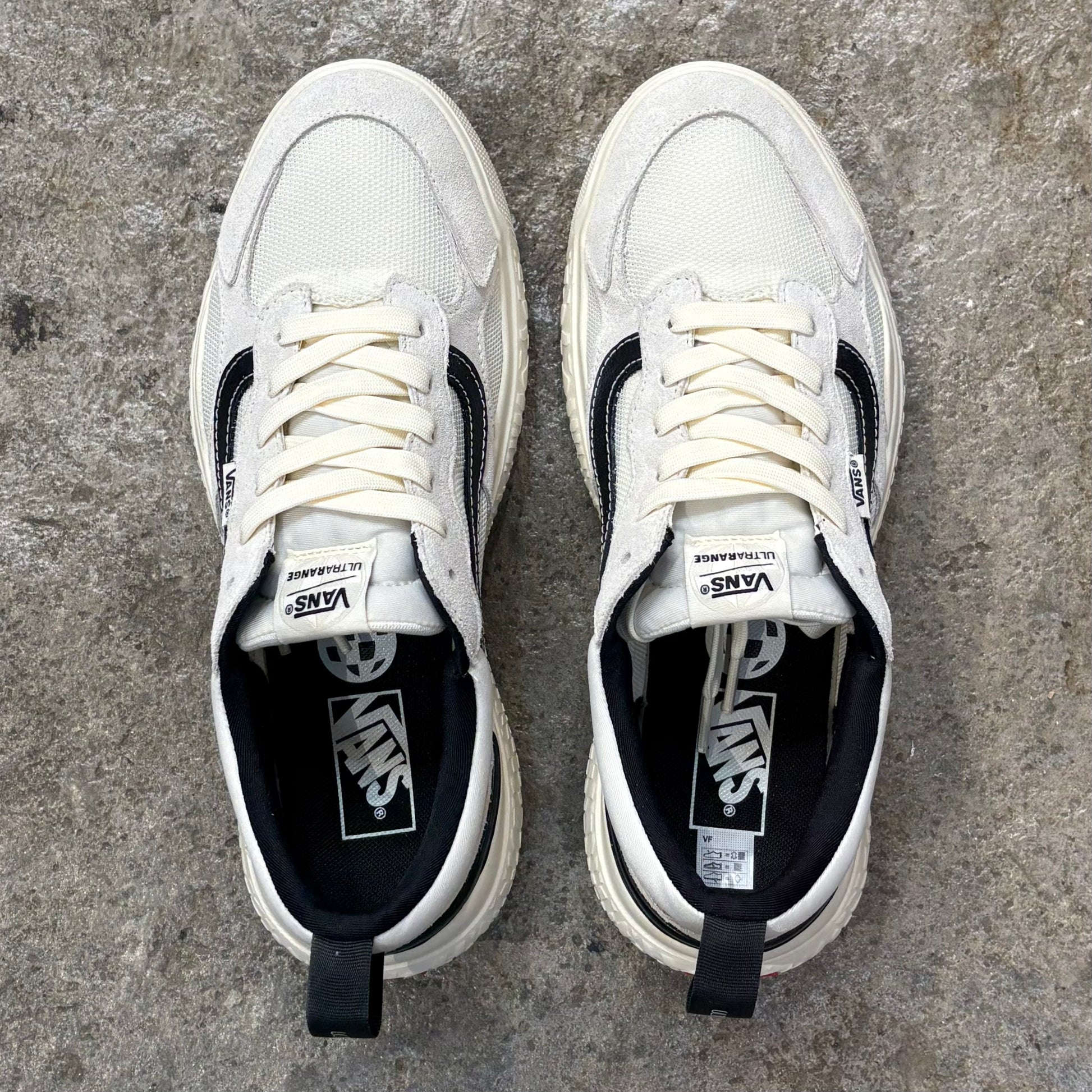 Pair of white sneakers with black accents on a concrete surface