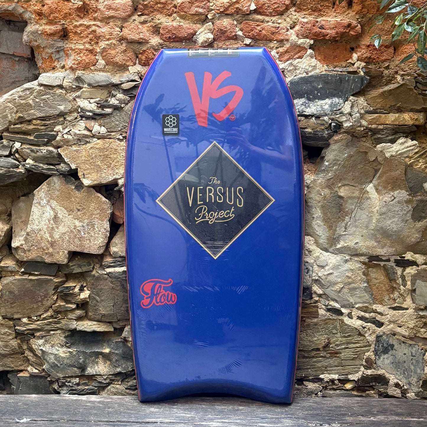 Blue bodyboard with red and gold branding against a stone wall
