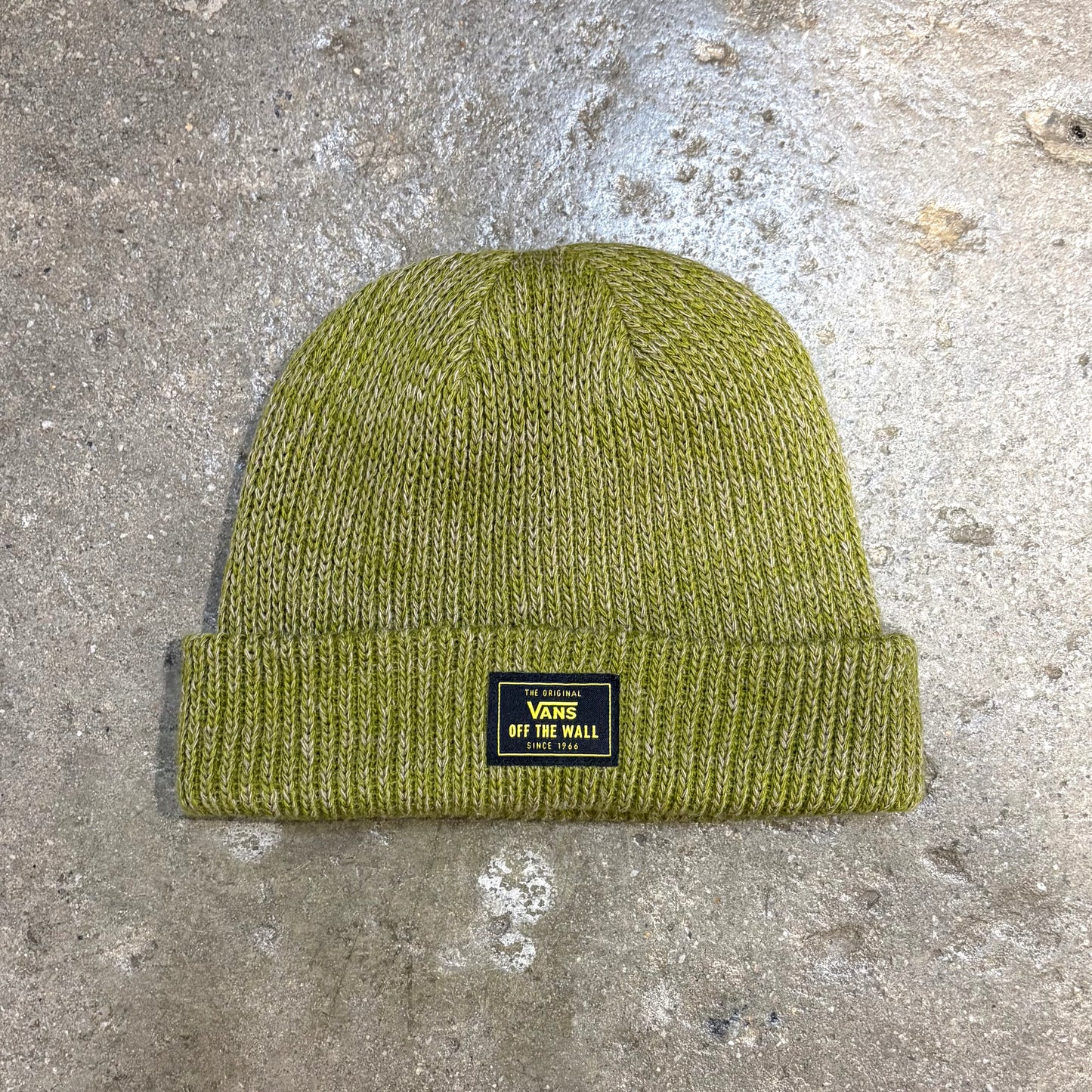 Green knit beanie with a Vans label on a concrete surface