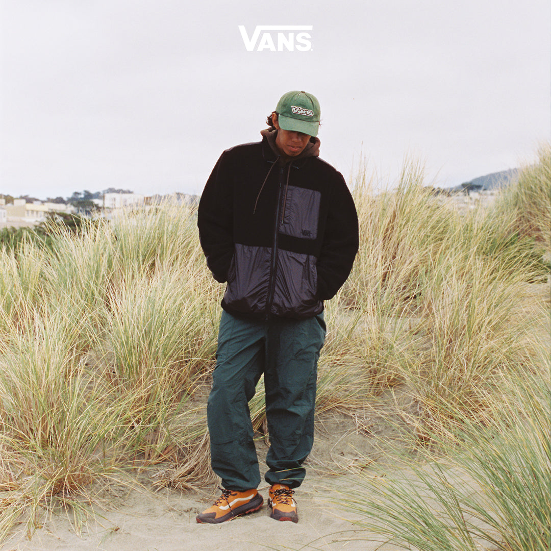 Man on a beach wearing Vans Crosspath in orange.