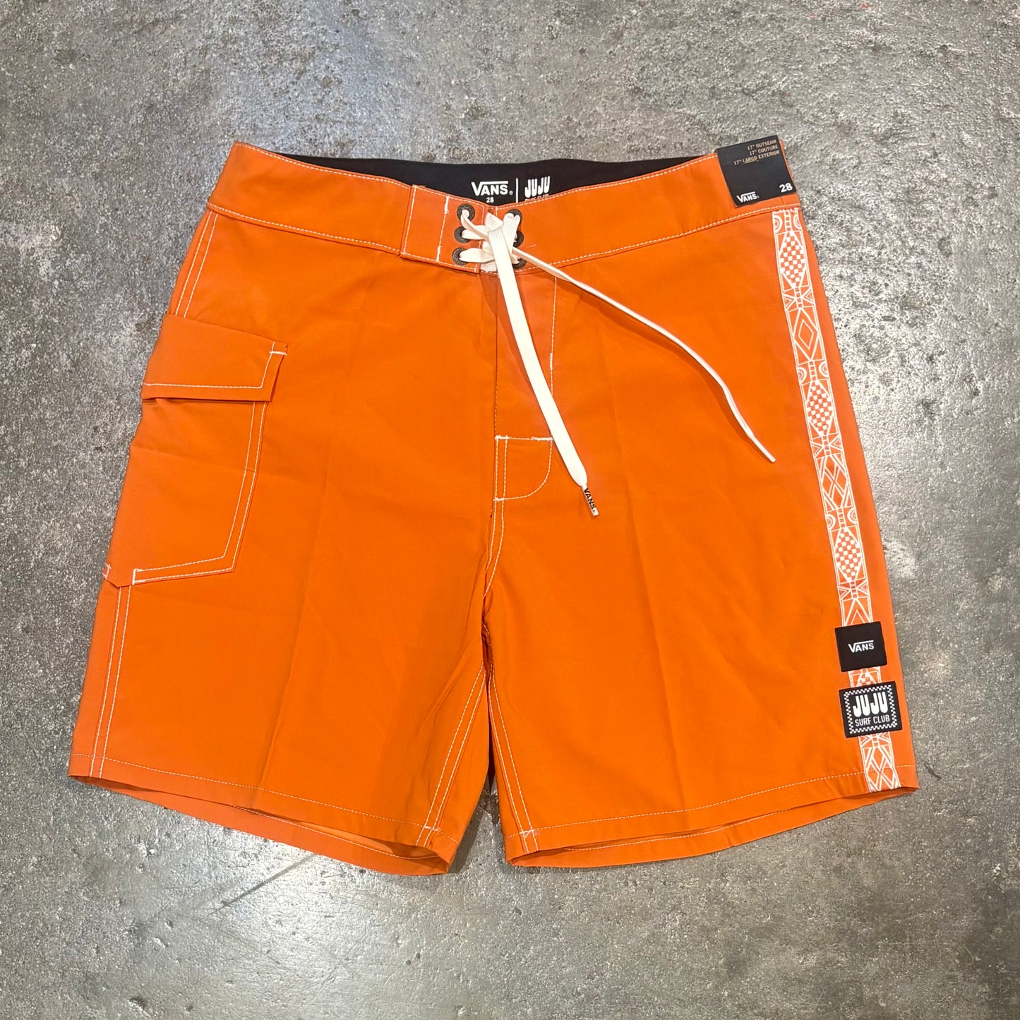 Orange shorts with white drawstring on a gray concrete surface